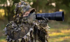 Fotograf w kamuflażu z liśćmi, z aparatem do fotografowania zwierząt, czeka na idealny moment do uchwycenia dzikiej przyrody.
