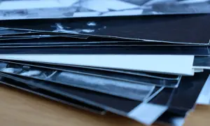 Stos czarno-białych odbitek, obraz fotograficzny na błonie światłoczułej, układa się na drewnianym blacie.