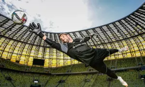 Bramkarz w locie łapie piłkę. Dynamiczna fotografia sportowa na tle stadionu.