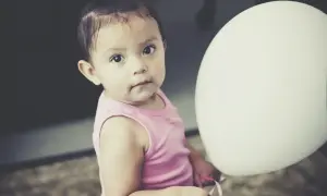 Urocza dziewczynka w różowej bluzeczce podczas sesji na roczek w domu, trzymająca biały balon.
