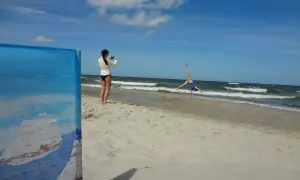Dziewczyna robi zdjęcie akrobatce na plaży. W tle widać morze i chmury, a horyzont jest lekko krzywy.