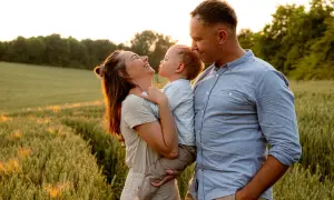 Szczęśliwa rodzina podczas sesji na łące. Mama śmieje się, trzymając dziecko, a tata patrzy na nich z czułością.