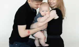 Szczęśliwa rodzina podczas sesji z niemowlakiem. Tata tuli dziecko, mama uśmiecha się.
