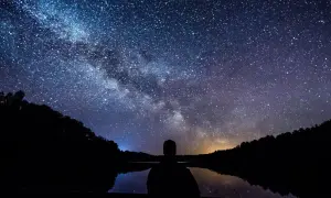 Sylwetka człowieka patrzy na Drogę Mleczną nad jeziorem. Idealny kadr, by pokazać, jak fotografować gwiazdy.