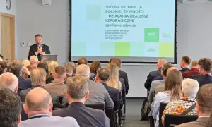 Mężczyzna przemawia na spotkaniu roboczym. Na ekranie widnieje napis "Spójna promocja polskiej żywności". Może to być wada obiektywu, która lekko zniekształca obraz.