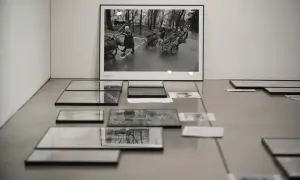 Wystawa prac Chrisa Niedenthala. Na ścianie wisi czarno-białe zdjęcie przedstawiające kobiety pchające wózki. Na podłodze leżą kolejne fotografie.
