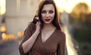 Piękna kobieta w brązowej sukience, z włosami opadającymi na ramię. Jej spojrzenie przyciąga uwagę w tej subtelnej fotografii portretowej.