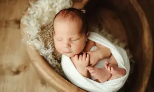 Urocze zdjęcia noworodków: śpiące maleństwo otulone białym kocykiem w drewnianej misie, otoczone miękkim futerkiem.