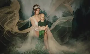 Ewa Miketa, niczym leśna nimfa, tuli chłopca w objęciach. Mglisty las i zwiewne tkaniny tworzą magiczną scenerię.