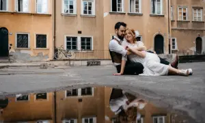 Kamil Włodarczyk i jego ukochana siedzą na ziemi, otoczeni starą kamienicą. Ich odbicie w kałuży dodaje magii tej chwili.