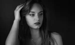 Portret młodej kobiety, fotografia czarno biała. Jej dłoń spoczywa na włosach, wzrok skierowany w bok, w zamyśleniu.