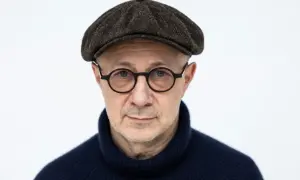 Mikołaj Grynberg w okularach i kaszkiecie, zamyślony, w granatowym golfie.