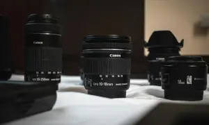 Kilka obiektywów Canon, w tym obiektyw standardowy 50mm i szerokokątny 10-18mm, leży na białej powierzchni.