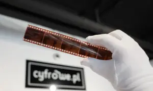 Biała rękawiczka trzyma pasek kliszy z widocznymi klatkami. To piękne zdjecia analogowe, które czekają na cyfrowe archiwum.