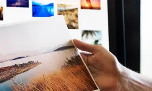 Ręka trzyma wydruk z krajobrazem, na ekranie widać kolejne zdjęcia do portfolio fotografa.