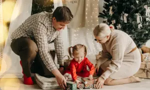 Wesoła sesja rodzinna w domu. Rodzice bawią się z córeczką zabawkami przy choince.