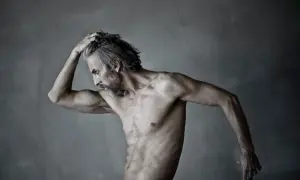Jacek Poremba, zamyślony, z ręką we włosach, na tle szarej ściany.