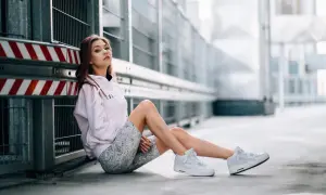 Młoda kobieta w różowej bluzie i wzorzystych legginsach siedzi na ziemi. To jeden z rodzajów portretów, ukazujący postać w miejskim otoczeniu.