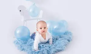 Uroczy niemowlak na niebieskim futerku, otoczony balonami. Idealny pomysł na sesję zdjęciową dziecka w domu.