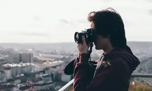 Przeswietlone zdjecie. Młody mężczyzna z aparatem fotograficznym w rękach, robiący zdjęcie miasta z góry.