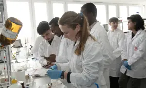 Monika Wanat i studenci w białych fartuchach pracują w laboratorium.