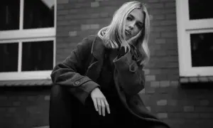 Blondynka w płaszczu opiera głowę na dłoni, zamyślona. Ten detal co to znaczy?