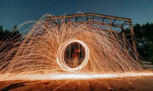Nocna fotografia z kręcącym się ogniem tworzącym świetlisty okrąg. To definicja kreatywnej fotografii.