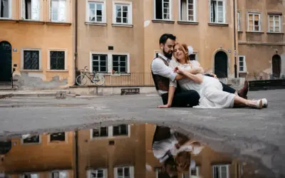 Kamil Włodarczyk i jego ukochana siedzą na ziemi, otoczeni starą kamienicą. Ich odbicie w kałuży dodaje magii tej chwili.
