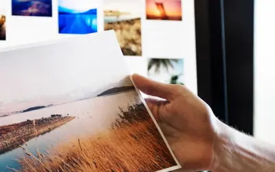 Ręka trzyma wydruk z krajobrazem, na ekranie widać kolejne zdjęcia do portfolio fotografa.