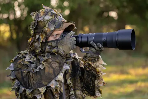 Fotograf w kamuflażu z liśćmi, z aparatem do fotografowania zwierząt, czeka na idealny moment do uchwycenia dzikiej przyrody.