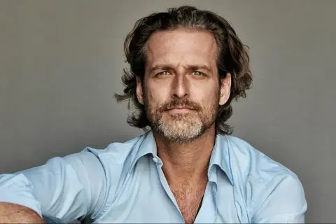 Portret mężczyzny o zielonych oczach i krótko przystrzyżonej brodzie, ubranego w błękitną koszulę. To Alexi Lubomirski.