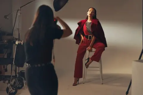 Modelka w czerwonym garniturze pozuje do zdjęć. Fotografka wykonuje zlecenia, łapiąc kadr.