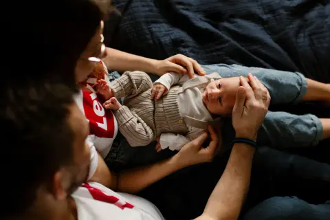 Ciepła sesja noworodkowa w domu. Rodzice czule trzymają swoje maleństwo, otulając je miłością.