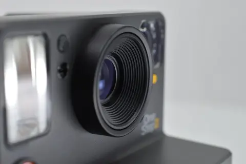 Zbliżenie na obiektyw aparatu Polaroid One Step 2. Widoczny błysk flesza i detale obudowy, sugerujące eksperymenty z bracketingiem ostrości.