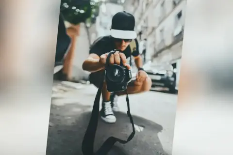 Młody fotograf w czapce z daszkiem trzyma aparat, gotowy do uchwycenia chwili. Zastanawiasz się, ile zarabia fotograf?