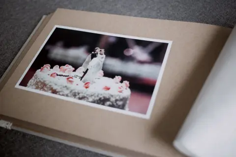 Otwarty album z fotografią tortu weselnego i figurkami pary młodej. Różne rodzaje papieru tworzą jego okładkę i strony.