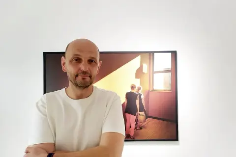 Krzysztof Gołuch obok swojego obrazu z kobietami niosącymi wiadra w świetle.