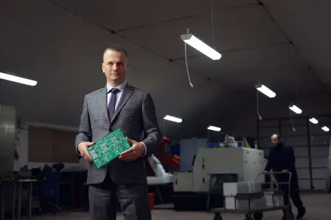Portret mężczyzny w garniturze trzymającego płytkę drukowaną. Wizerunek inaczej ukazuje jego rolę w branży technologicznej.