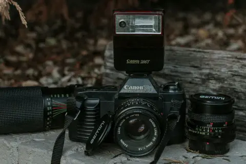 Stary aparat Canon 750 z lampą błyskową Canon Speedlite 244T i obiektywami. Lampa błyskowa inaczej niż współczesne, to retro sprzęt.