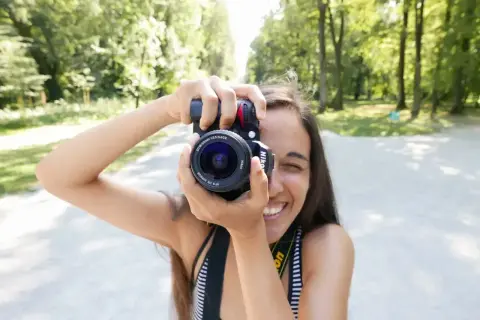 Uśmiechnięta dziewczyna z aparatem i obiektywem 18-55, idealnym do krajobrazów i portretów w plenerze.