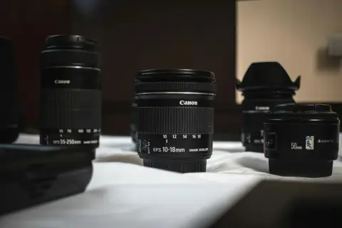 Kilka obiektywów Canon, w tym obiektyw standardowy 50mm i szerokokątny 10-18mm, leży na białej powierzchni.