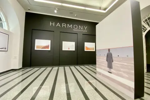 Wystawa "HARMONY" Marcina Ryczka. W galerii widzimy fotografie mnichów i dużą instalację z podobizną postaci w szarym płaszczu.