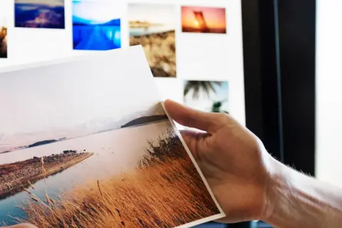 Ręka trzyma wydruk z krajobrazem, na ekranie widać kolejne zdjęcia do portfolio fotografa.