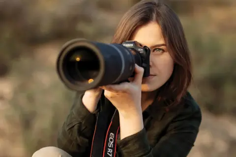 Kobieta z aparatem Canon EOS R7 w rękach, gotowa do uchwycenia idealnego ujęcia. Jej skupienie zdradza pasję do fotografii mody.
