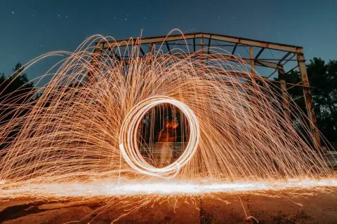 Nocna fotografia z kręcącym się ogniem tworzącym świetlisty okrąg. To definicja kreatywnej fotografii.