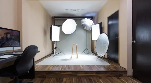 Gotowy pokój fotografa: lampy, statywy, taboret i komputer czekają na sesję.