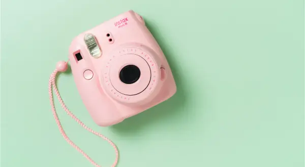 Różowy aparat Instax Mini 8 na pastelowym tle. Dowiedz się, jak działa Instax, tworząc natychmiastowe zdjęcia.