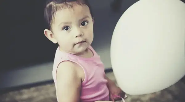 Urocza dziewczynka w różowej bluzeczce podczas sesji na roczek w domu, trzymająca biały balon.