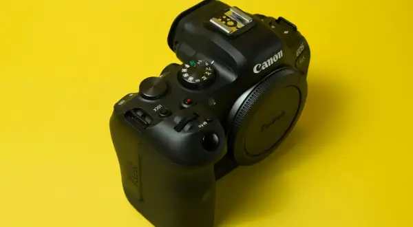 Czarny aparat Canon EOS R6 na żółtym tle. Pokrętło trybów pozwala na preselekcję czasu, ułatwiając kontrolę nad ekspozycją.