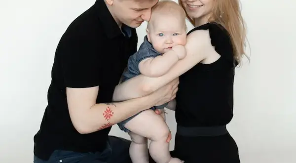 Szczęśliwa rodzina podczas sesji z niemowlakiem. Tata tuli dziecko, mama uśmiecha się.